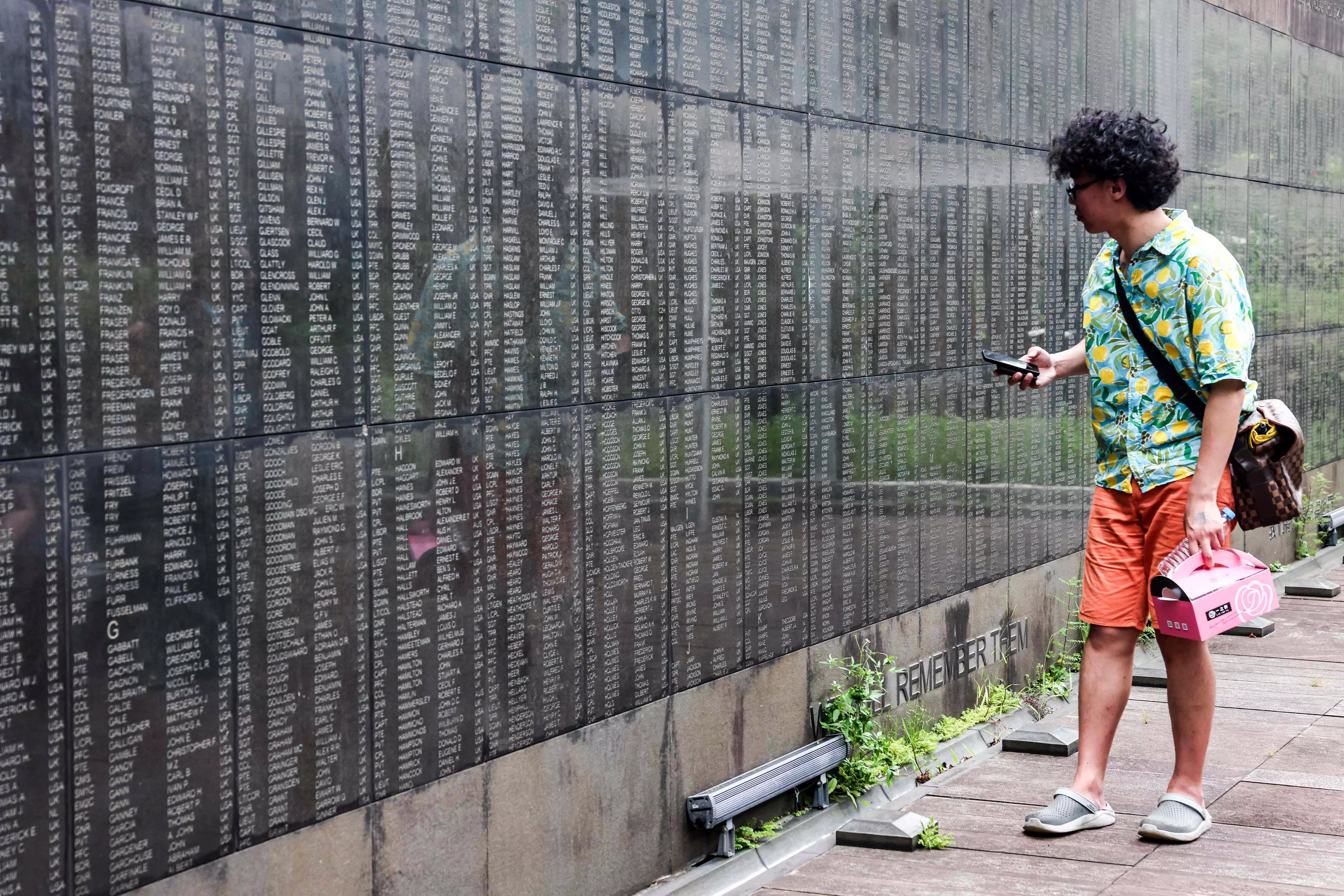 A man walks past a list of names of Prisoners of War (POW) from WWII seen at Taiwan POW Memorial and Peace Park in New Taipei City on July 31, 2025. In a small urban park in Taiwan, more than 4,000 names are etched into a granite wall -- most of them British and American servicemen held by the Japanese during World War II. (Photo by I-Hwa Cheng / AFP) 
